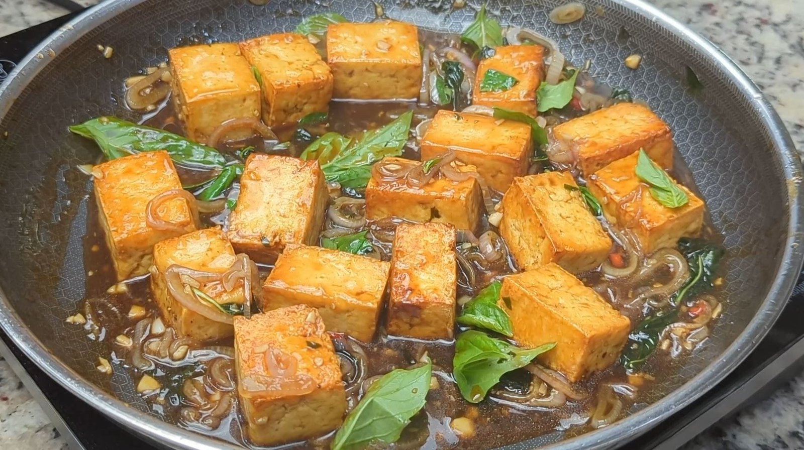 Cubes of Tofu braised in a thai basil sauce in frying pan