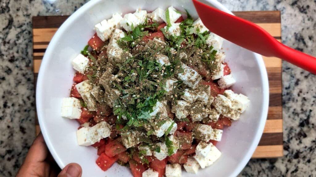Mixing ingredients for watermelon feta salad in a large salad bowl