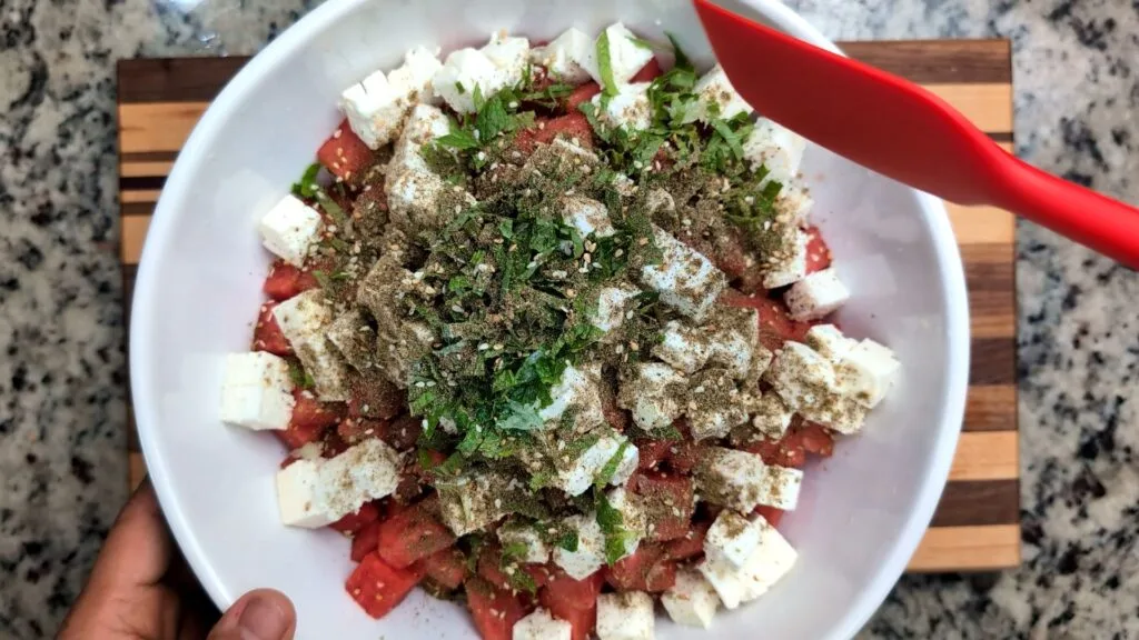 Mixing ingredients for watermelon feta salad in a large salad bowl
