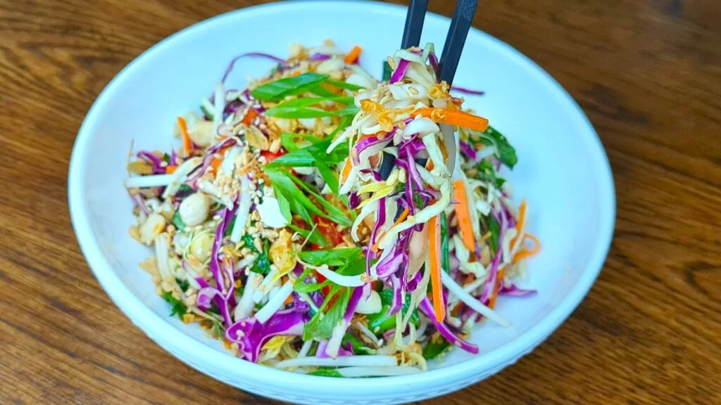 enjoying Asian Coleslaw in a white bowl and black Chopsticks