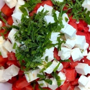 Watermelon and Feta cubes with mint leaves on top in a white salad bowl