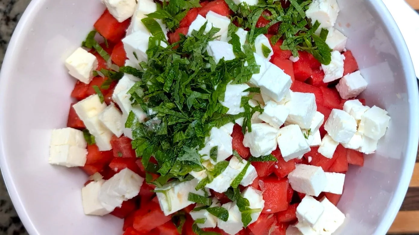 Watermelon and Feta cubes with mint leaves on top in a white salad bowl