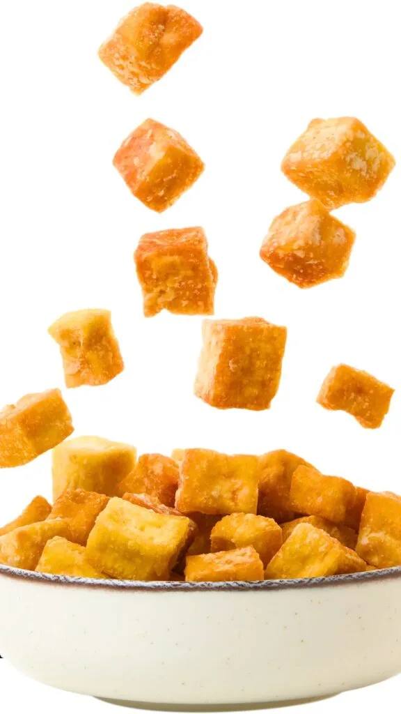 Fried Tofu dropping into a white bowl - vertical