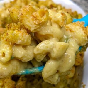 Creamy Vegan Mac and cheese being lifted from a baking pan with a large spoon