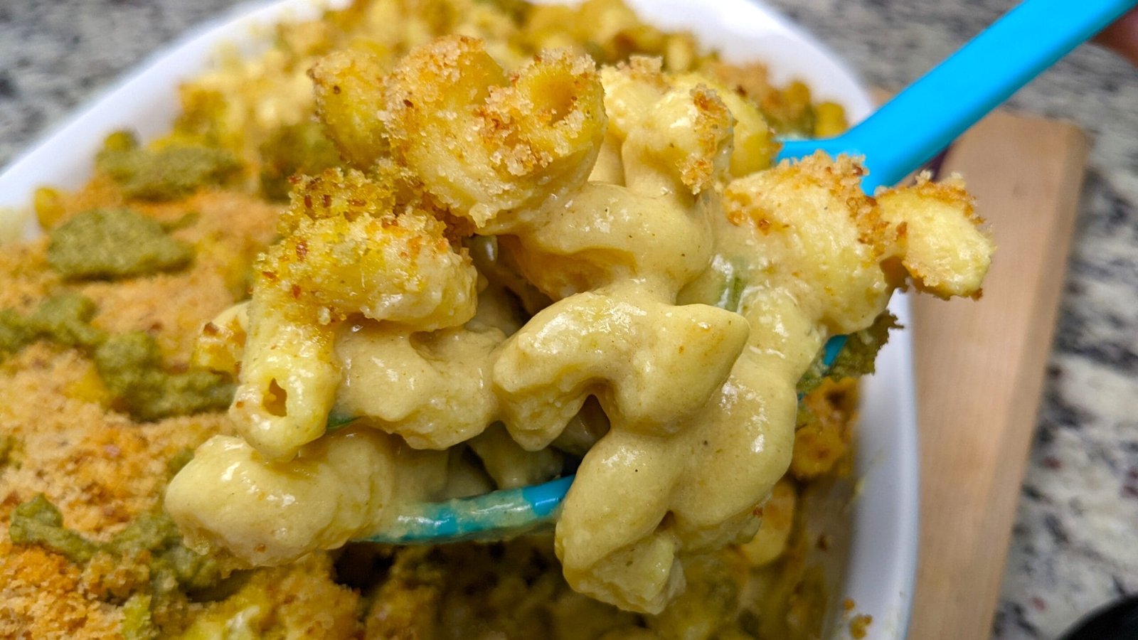Creamy Vegan Mac and cheese being lifted from a baking pan with a large spoon