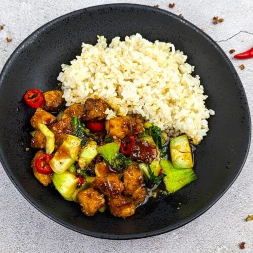 Sichuan Tofu Stir Fry served with steamed brown rice in a black bowl