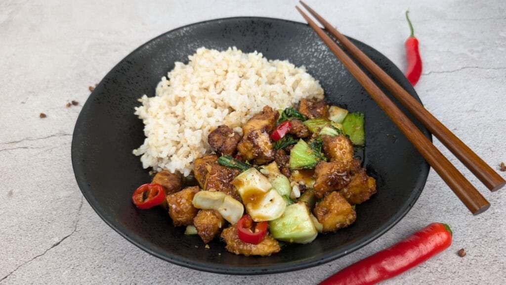 Sichuan Tofu Stir Fry served with steamed brown rice in a black bowl