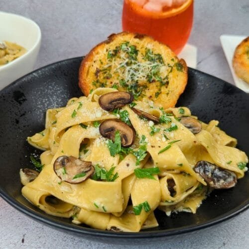 Mushroom Pappardelle Pasta served in a black bowl with garlic bread