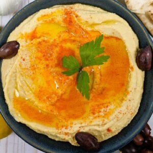 Creamiest Hummus served in a blue bowl with olives and bread